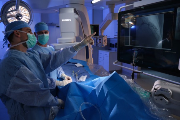 Two surgeons look at a video screen showing an internal image of a body. 